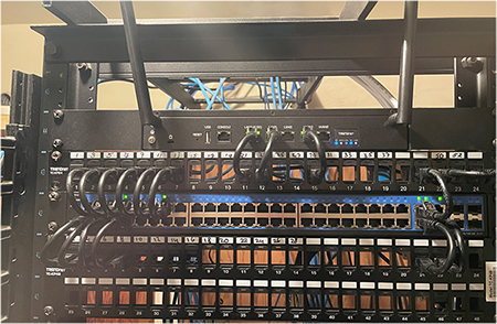 Una configuración de rack de red muestra un conmutador y dos paneles de conexión con puertos numerados, todos conectados por cables Ethernet cuidadosamente agrupados enrutados a través de barras de administración de cables, lo que ilustra un sistema de cableado estructurado y profesional.