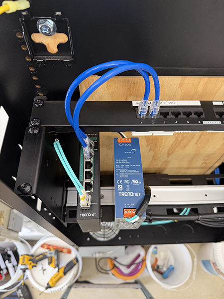A network rack setup displays a switch and two patch panels with numbered ports, all connected by neatly bundled Ethernet cables routed through cable management bars, illustrating a structured and professional cabling system.