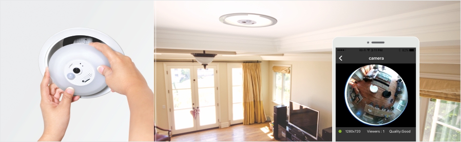 A person installs a round, white device into a ceiling fixture, which appears to be a security camera. The room includes large windows with curtains, a ceiling light fixture, a television, and furniture. An inset on a smartphone screen displays a live feed from the camera, showing a fisheye view of the room.