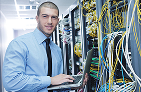 La ilustración muestra a un hombre sosteniendo una computadora portátil en una sala de servidores con múltiples cables visibles.