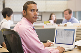 Four individuals working at desks with computers in a modern office setting. Highlighting the use of technology and collaborative workspaces in a professional environment.