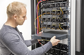 A person installs hardware into an open server rack filled with cables and other equipment.